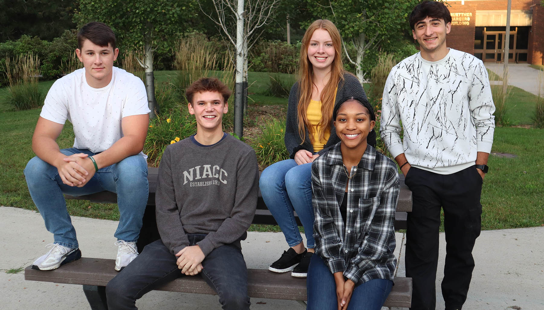 College students smiling while sitting and standing at a picnic bench